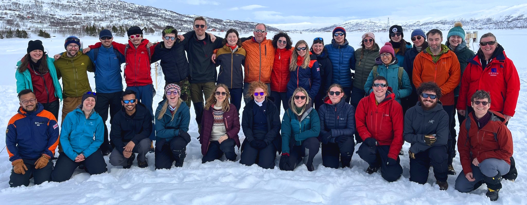 The attendees and instructors of the CryoSkills course, 2024 stand as a group in front of a snowy background.